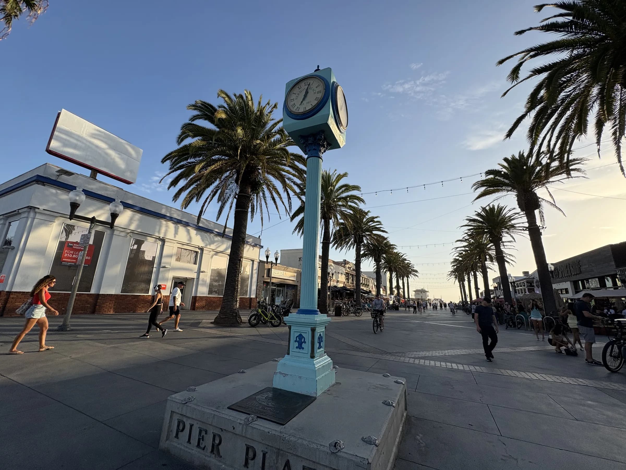 The clock and Pier Plaza marker beneath tall palm trees