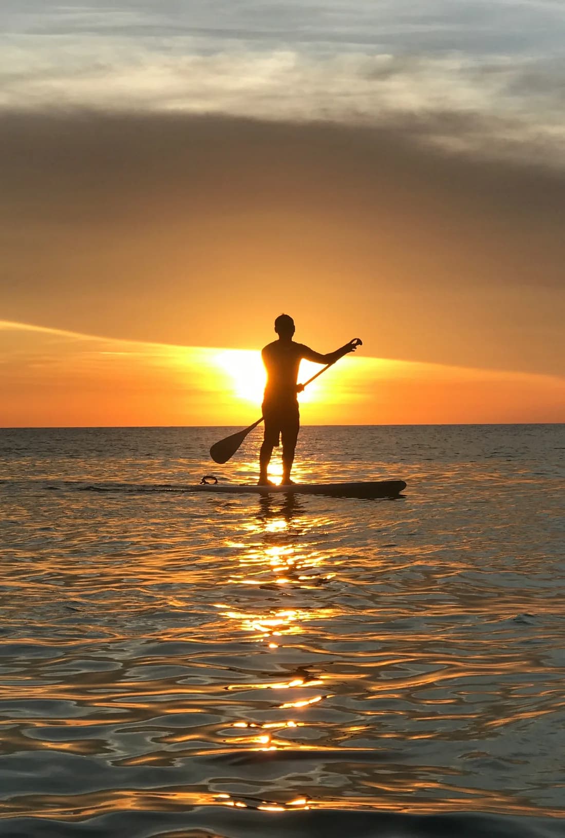 A lone paddleboarder silhouetted against a warm sunset