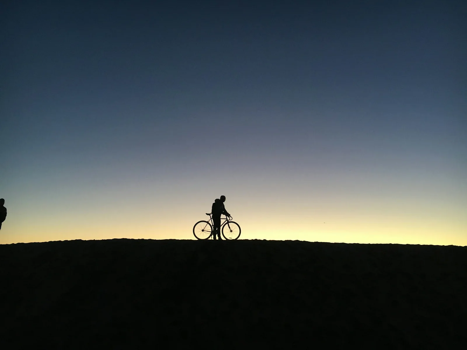 A cyclist silhouetted at sunset along a South Bay beach path