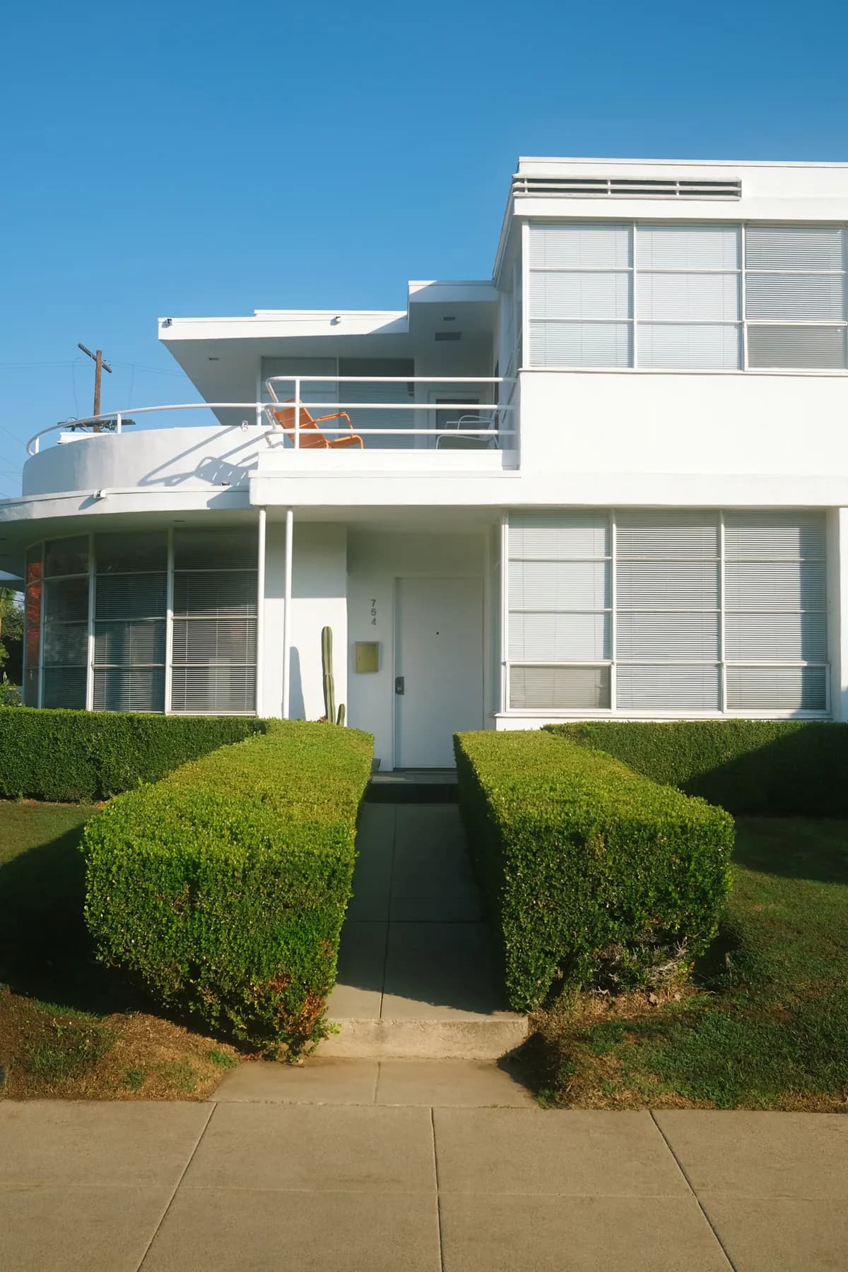 A white Southern California home with clipped hedges and a sunny sidewalk