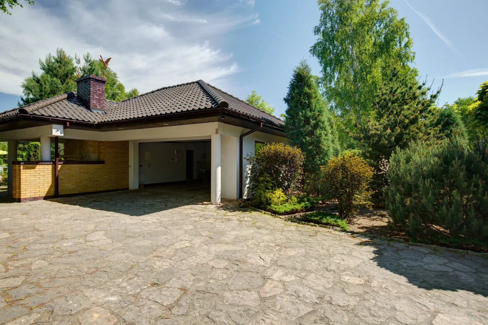 A low-rise tile-roof home framed by a driveway and mature landscaping