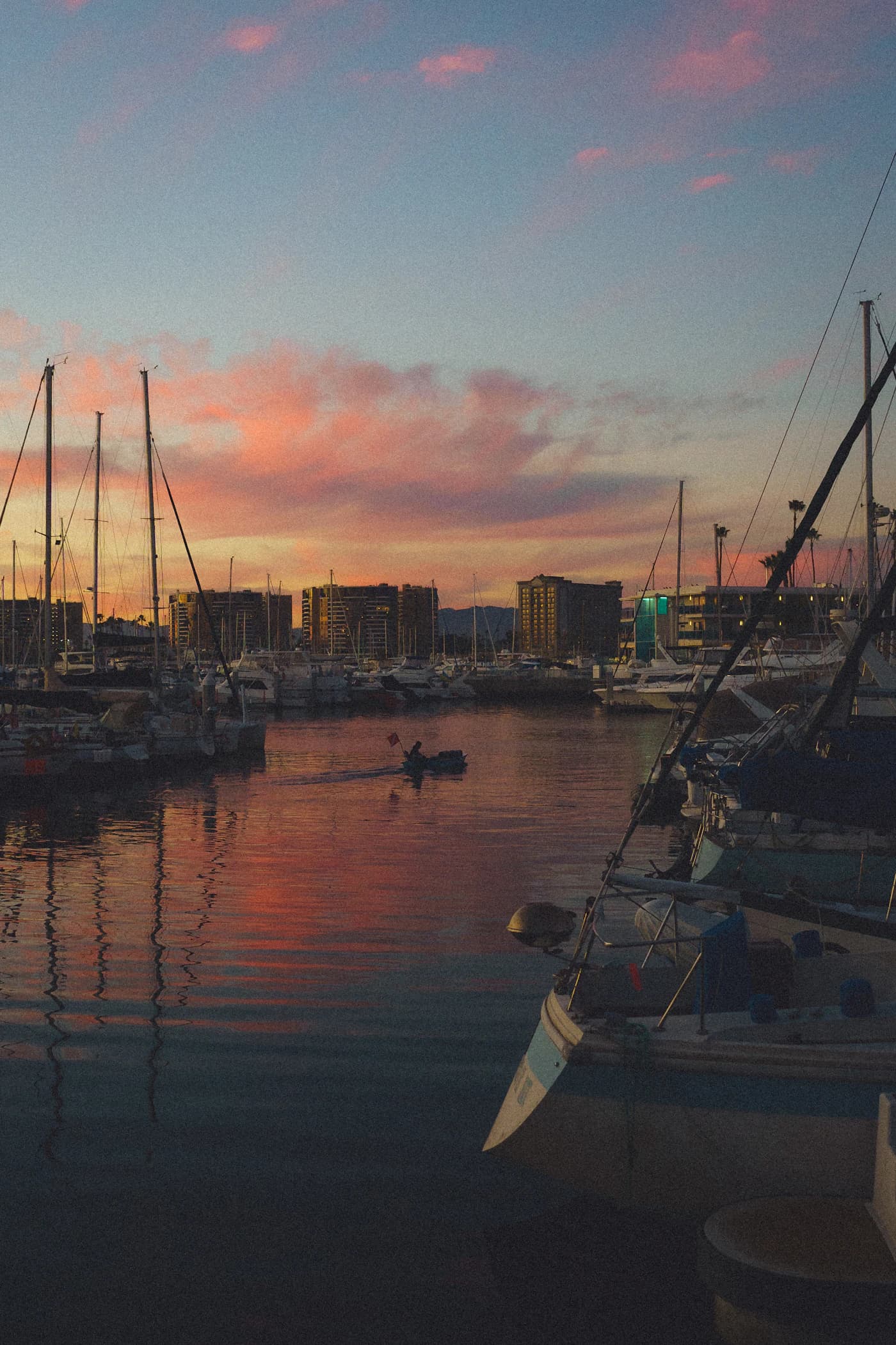 A sailor crossing a pink Marina del Rey sunset between moored boats
