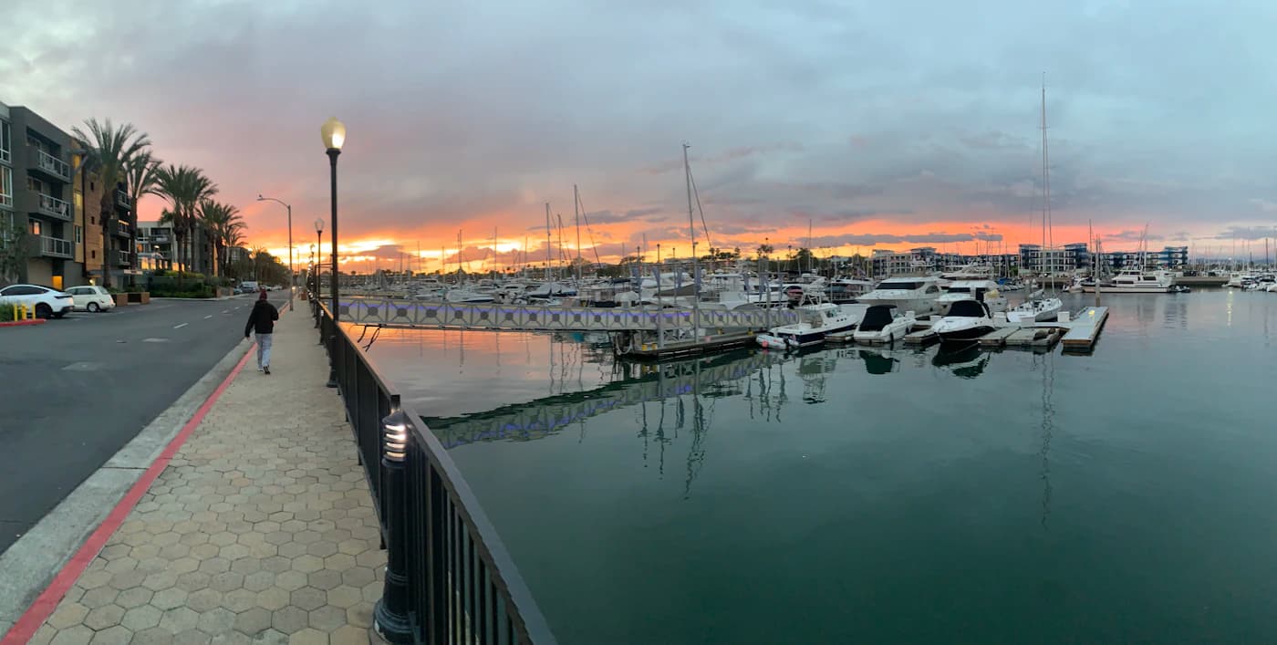A person walking the Marina del Rey harbor promenade at sunset