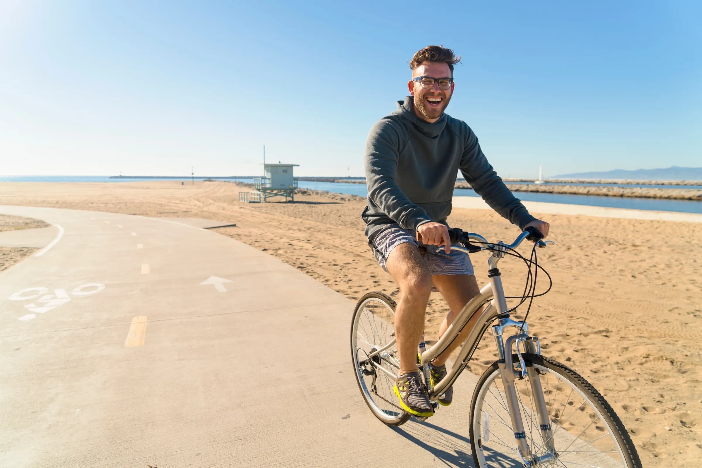 A cyclist riding a paved path beside a wide sandy beach