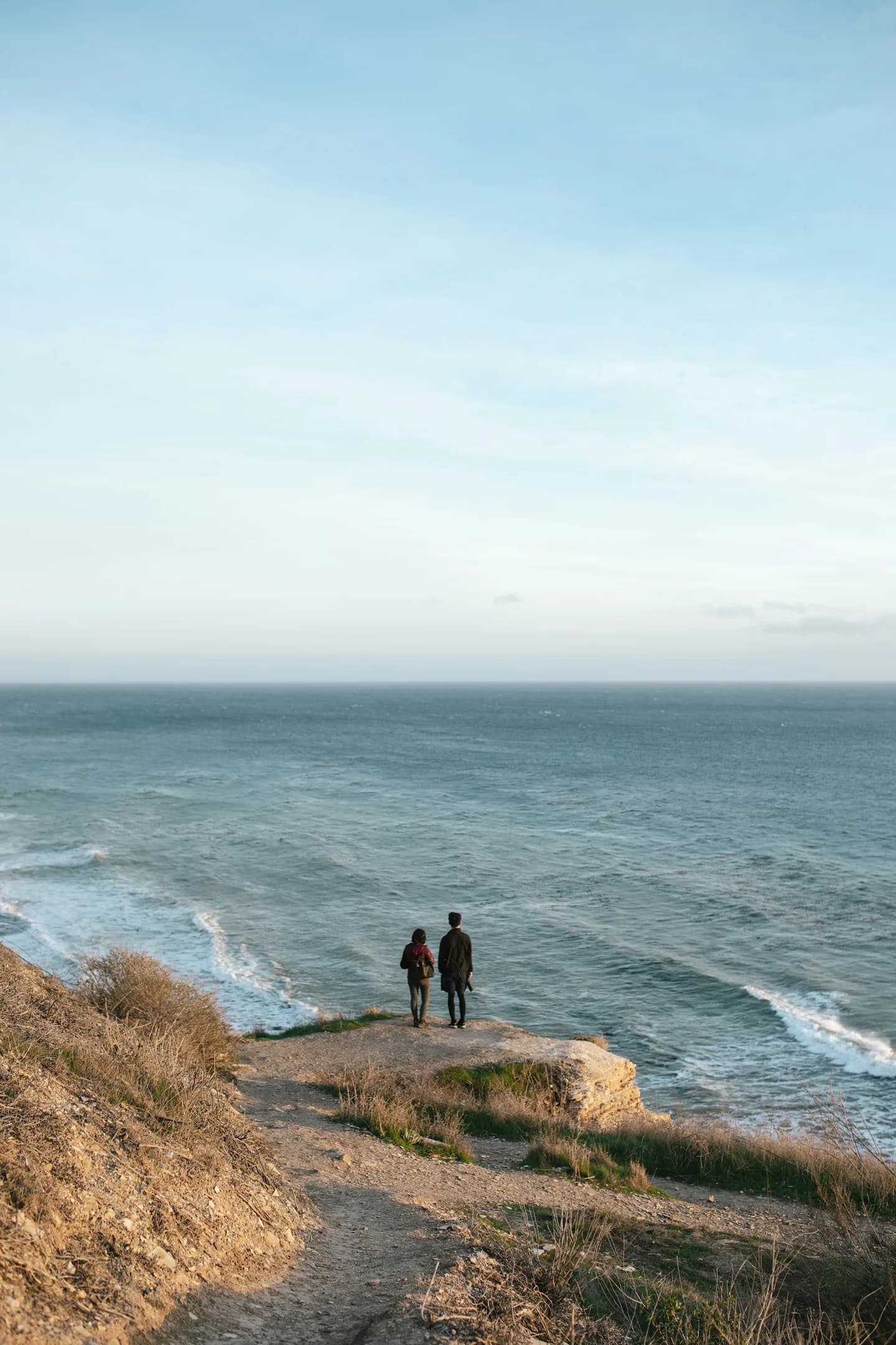 Two walkers pausing together at the edge of a coastal bluff