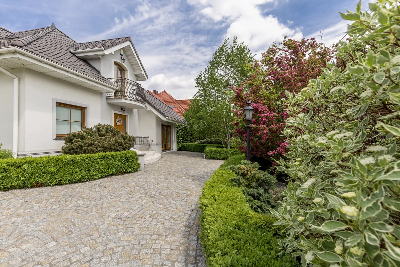 A white stucco residence with a tiled roof, landscaped driveway, and flowering shrubs