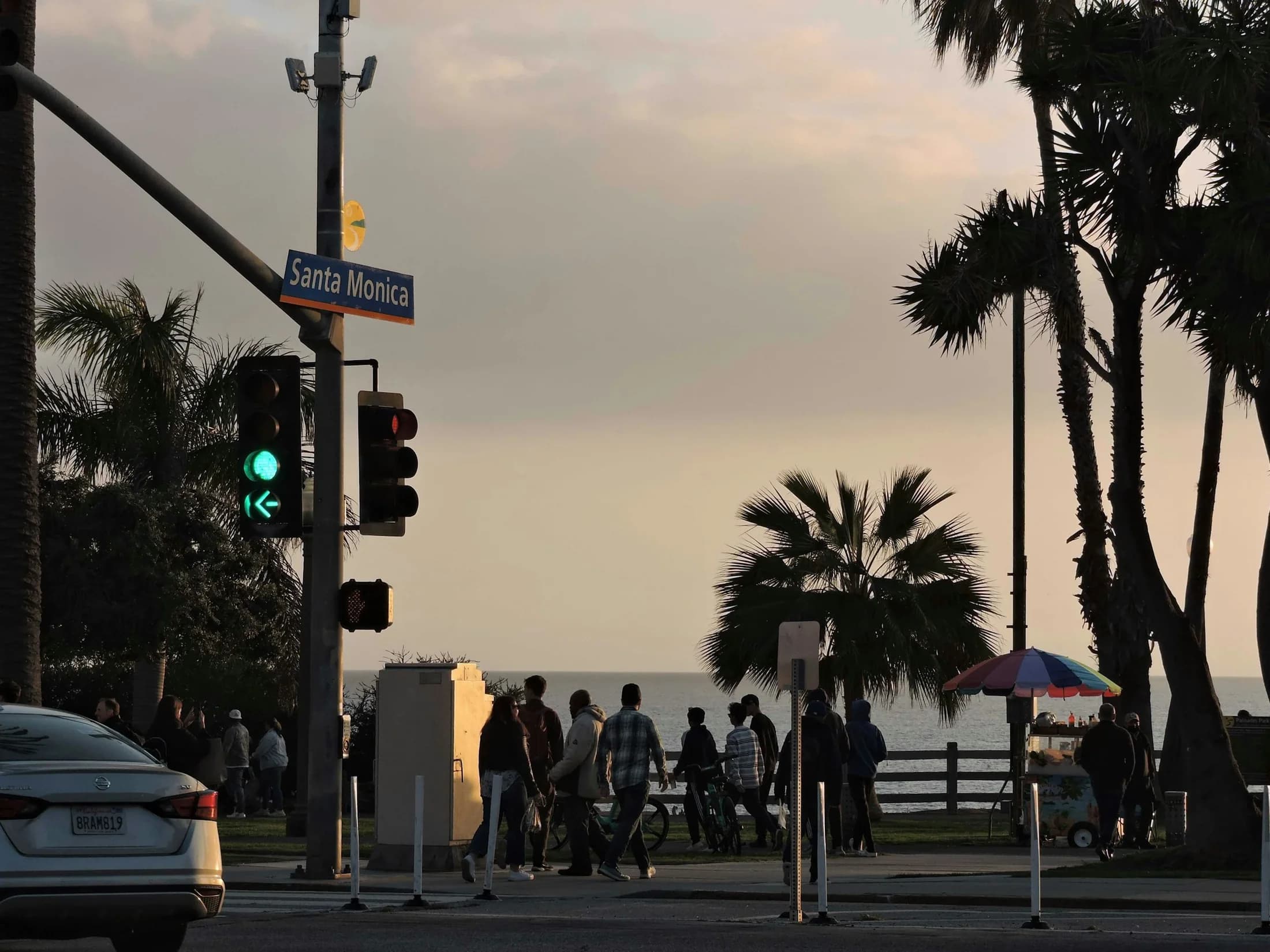 Pedestrians crossing a palm-lined Santa Monica intersection in evening light