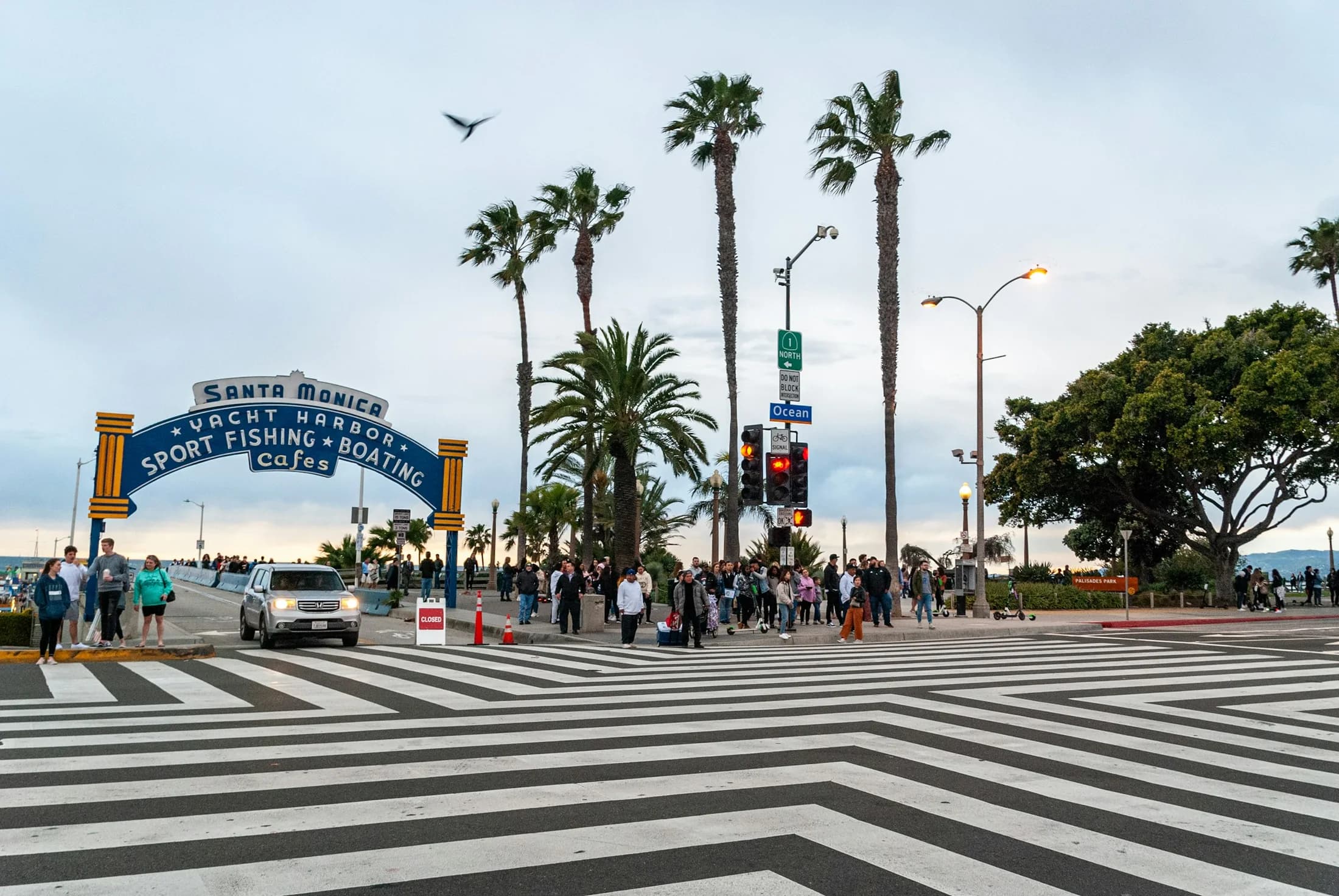 The blue Santa Monica Pier arch beyond a broad striped crosswalk