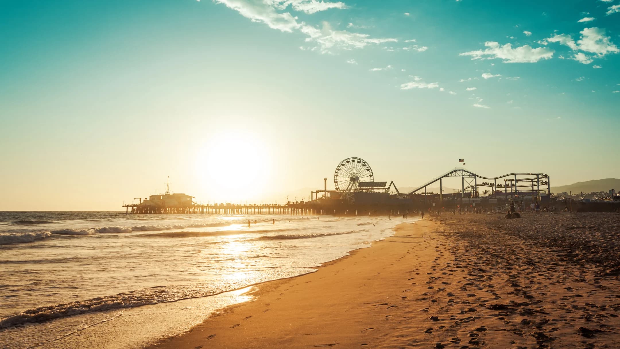 Santa Monica Pier and Pacific Park glowing beside the shoreline at sunset