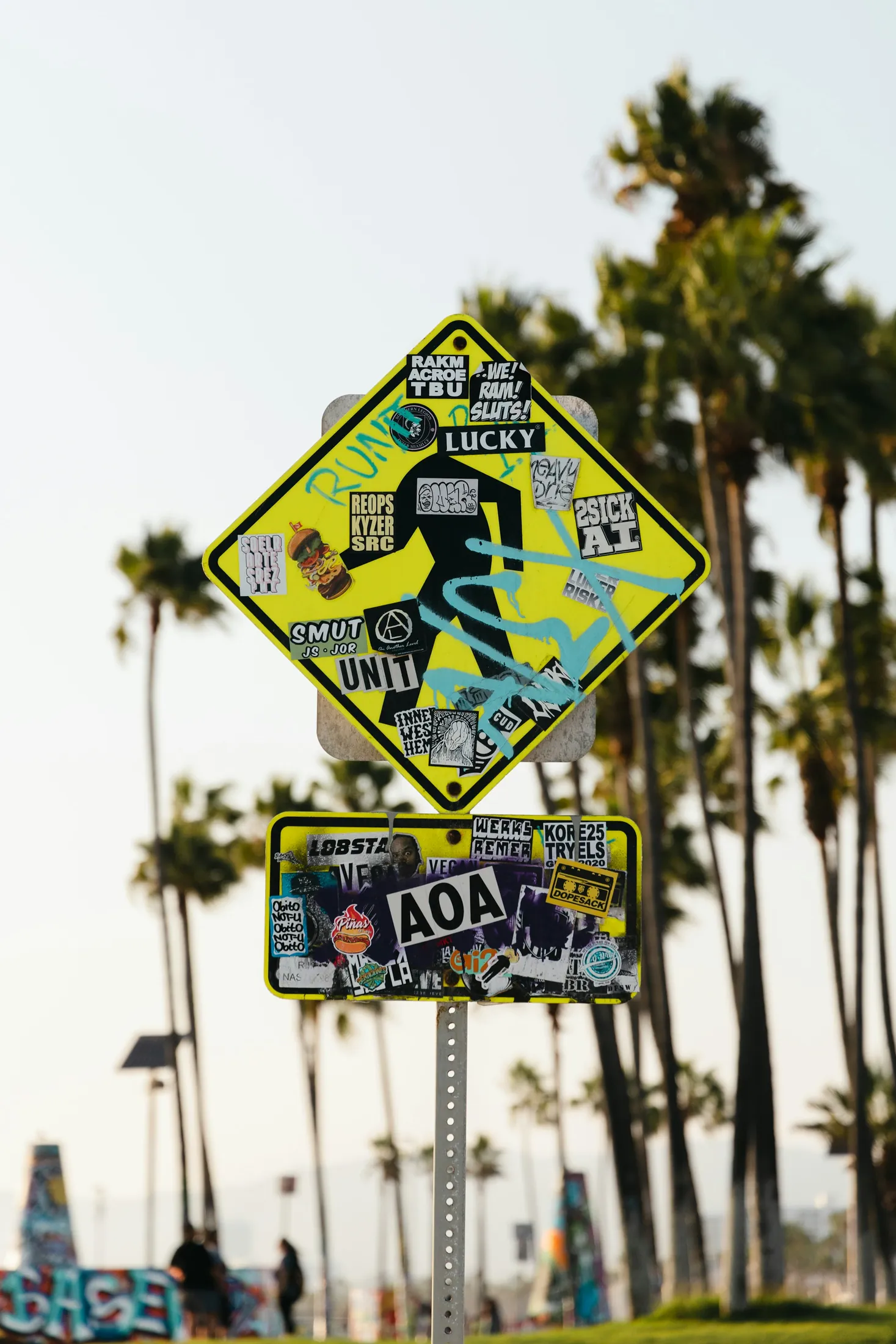 A Venice Beach sign layered with stickers against palms and sky