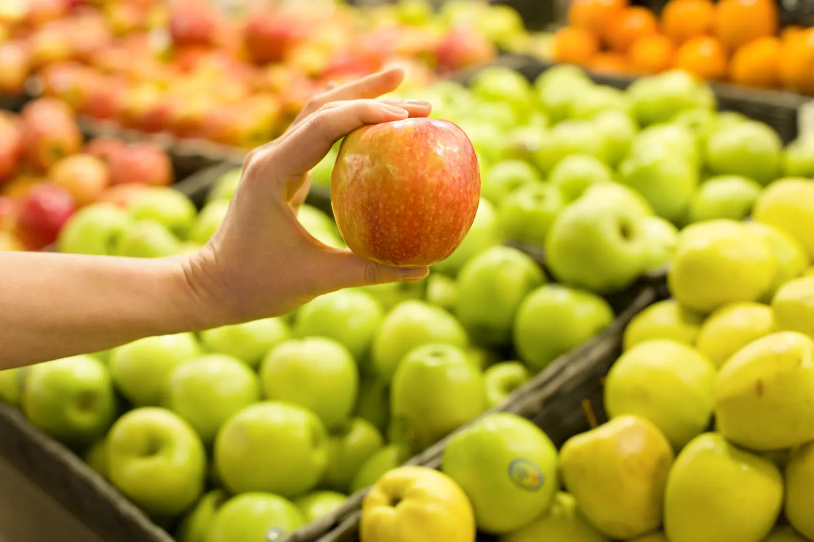 A shopper selecting apples from a colorful produce display